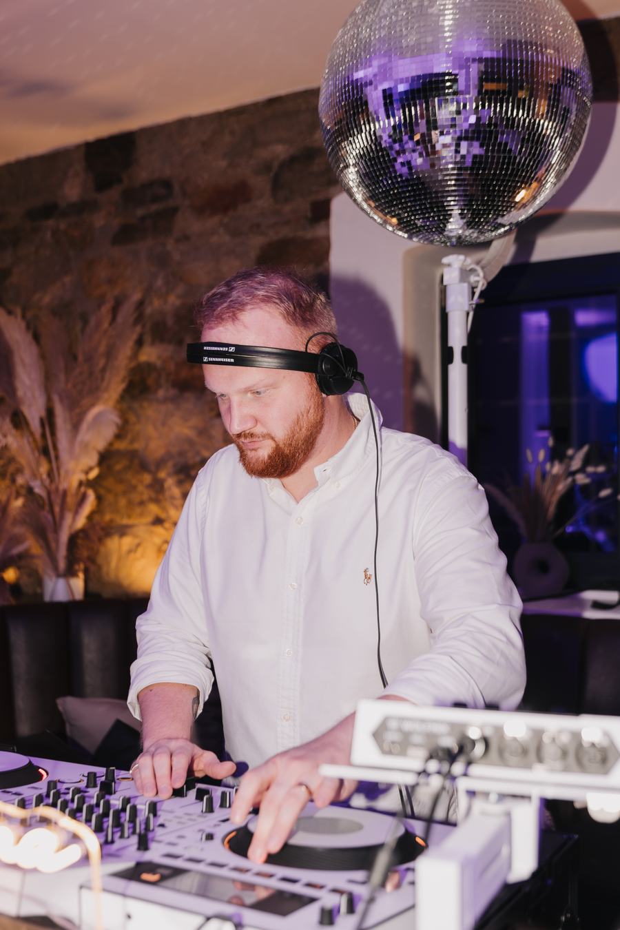 James Kuma an den Decks unter der Discokugel, warmes Licht vor einer Natursteinwand